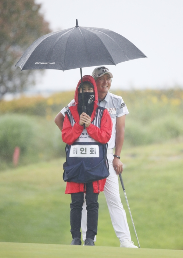 허인회(뒤) 프로와 아내인 육은채 캐디가 비 내리는 필드에서 함께 우산을 쓰고 있다. /KPGA 제공