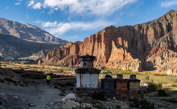 무스탕의 대표 풍경 중의 하나인 닥마르 마을의 붉은 절벽과 공중동굴. 마을 입구에 서 있는 불탑 옆으로 트래커가 지나가고 있다.