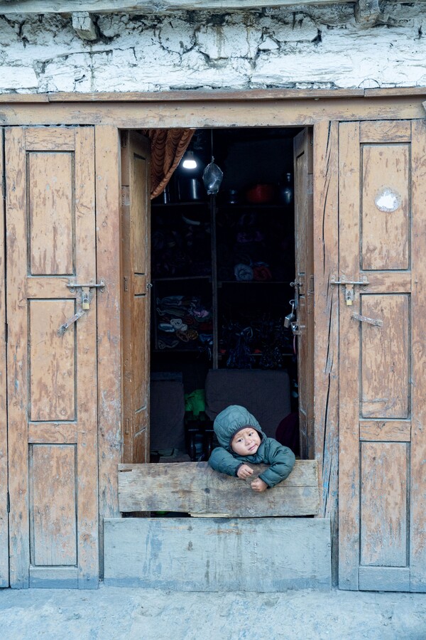 도로가 티베트 전통가옥의 대문에 걸터앉아 밖을 보고 있는 어린아이.