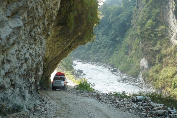 깎인 바위 밑 도로를 지나는 자동차. 좀솜까지 무너지고 패인 험한 산악도로가 계속 이어진다.