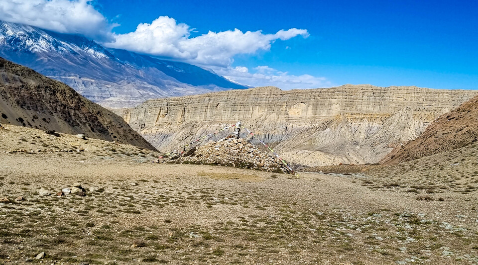 널찍한 고개 정상에 있는 돌무더기에 매달린 룽다와 타루쵸. 계곡 건너편에 만리장성 같은 절벽이 병풍을 두르고 있다.