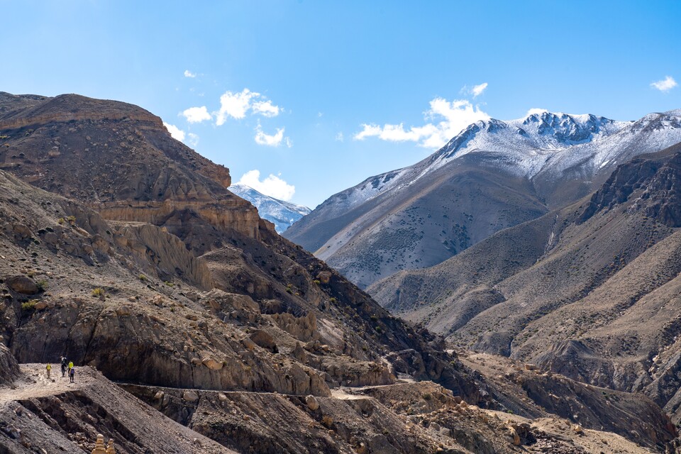 트레커들이 계곡 사이 산 사면으로 끝없이 이어지는 벼랑길을 따라 걷고 있다.