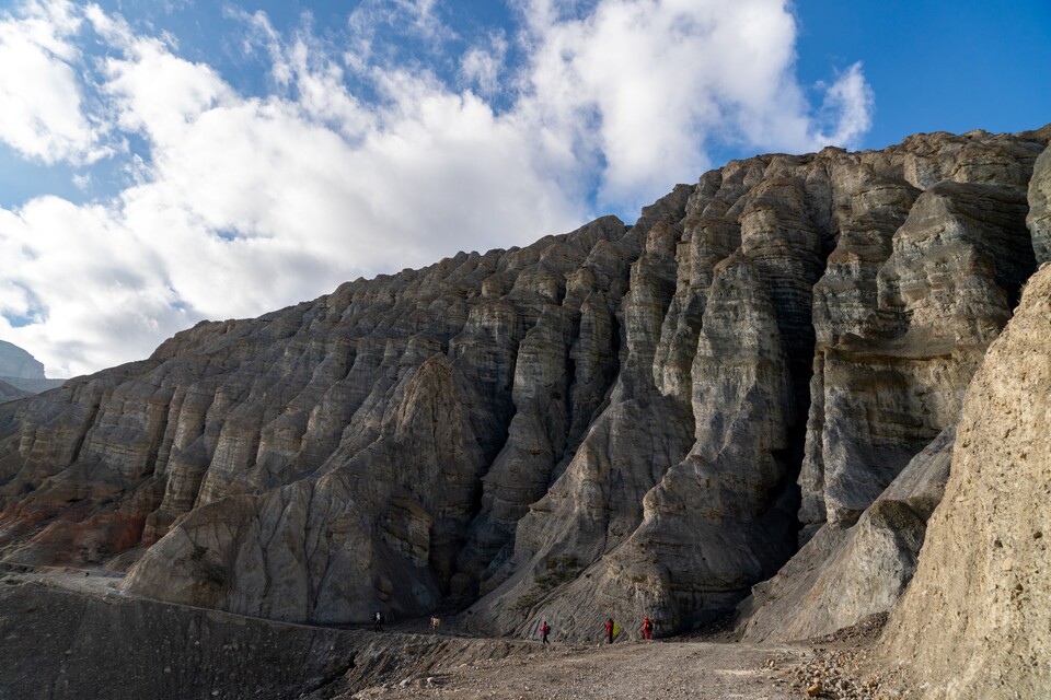 트레커들이 SF영화에 나오는 외계행성의 모습 같은 거친 바위 절벽 아래를 걷고 있다.