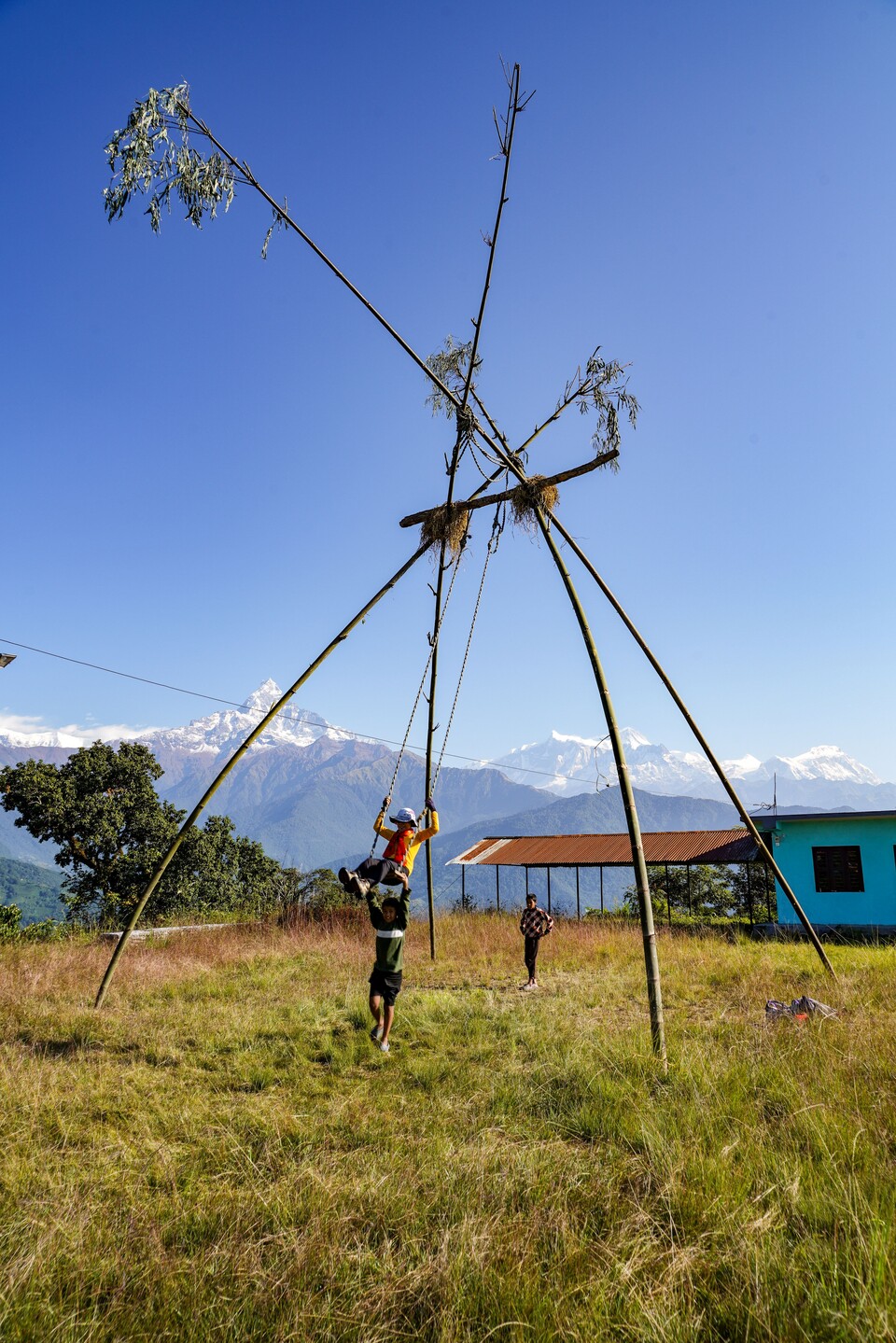 동료가 휴식시간에 마을 입구에 설치된 키큰 대나무를 엮어 만든 그네를 타며 허공을 가르고 있다.