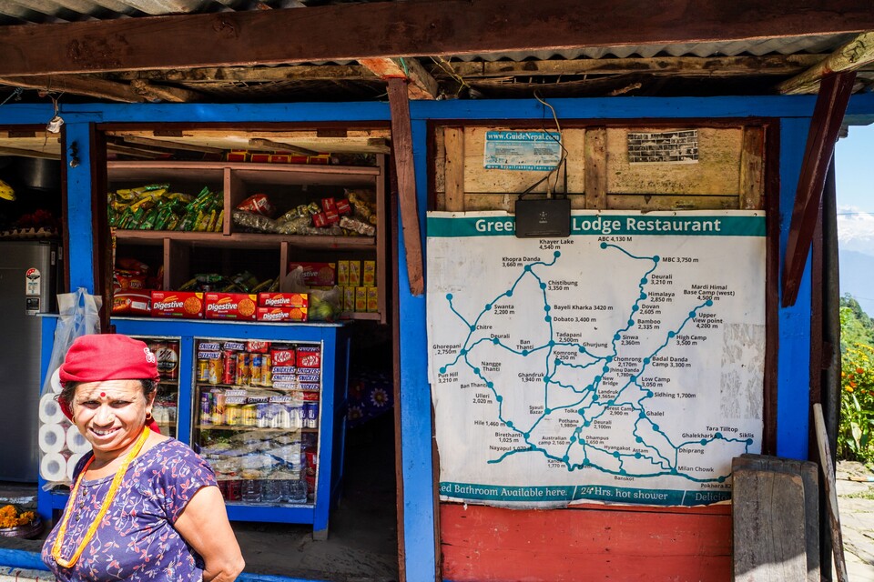 안나푸르나 산군의 거미줄 같은 트레일 루트 지도가 붙어있는 구멍가게 앞에서 동네 아낙이 웃고 있다.