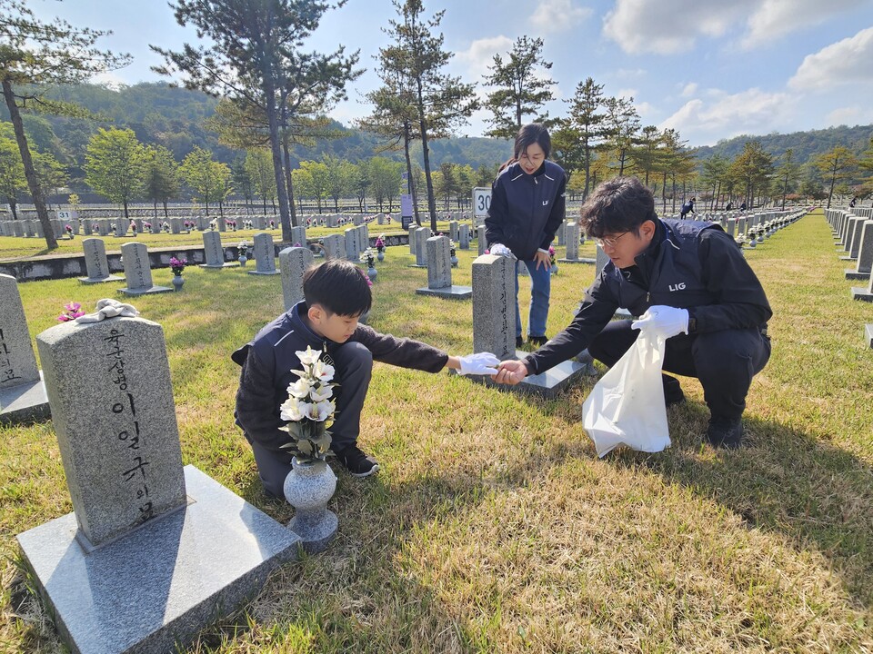 LIG넥스원 직원 가족이 지난 25일 국립서울현충원 30묘역에서 묘역 단장 봉사활동을 펼치고 있다./LIG넥스원