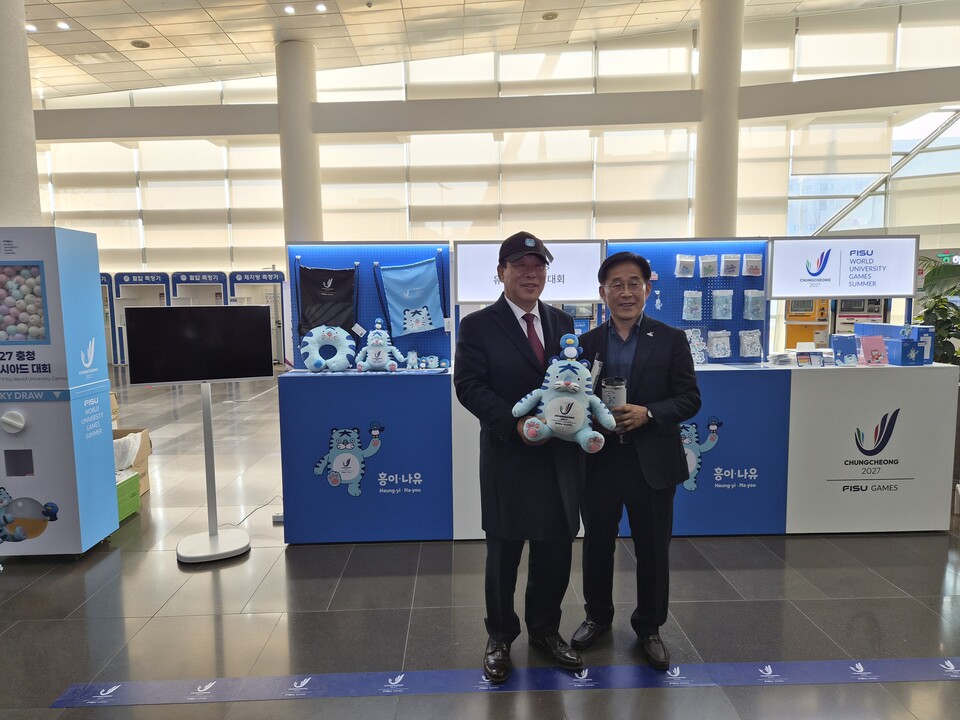 2027 충청 유니버시아드대회 조직위원회가 24일 세종시청 1층 로비에 공식 상품 팝업 부스를 설치하고 20여 종의 굿즈를 선보이는 이벤트를 개최했다. 행사장을 찾은 최민호 세종시장과 조직위 이창섭 부위원장이 굿즈를 들고 기념촬영을 했다. / 조직위 제공