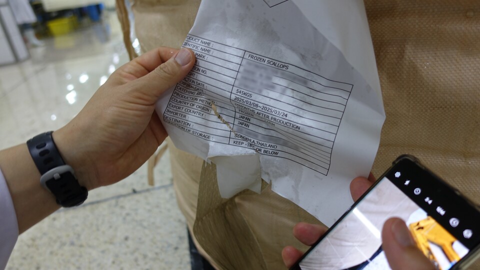 대형자루 태그에 원산지가 일본산 가리비로 명시된 것을 확인하는 모습. 사진